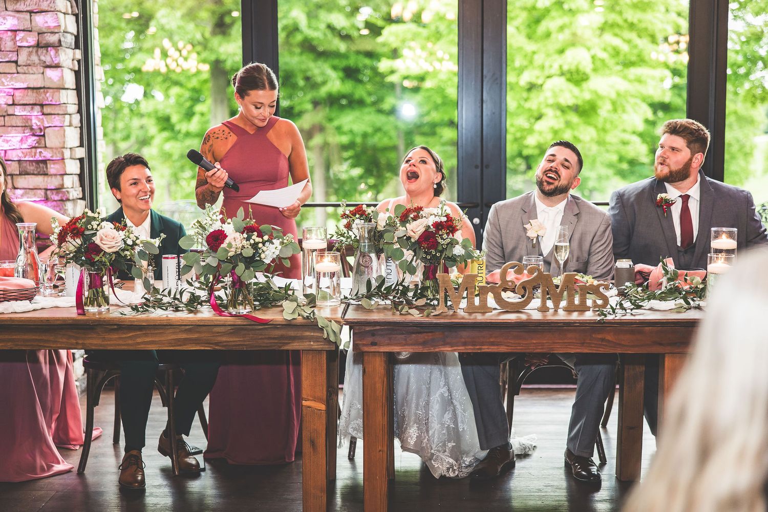 Wedding reception head table decorated with lush floral arrangements and greenery.