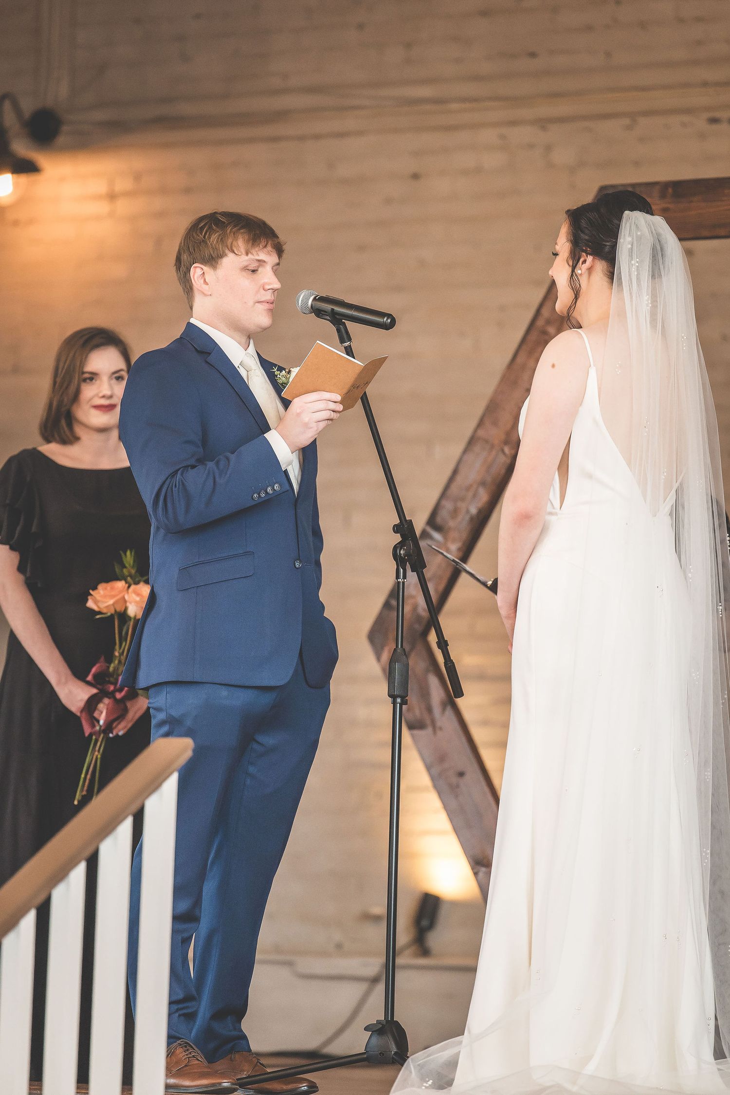 Wedding ceremony moment captured in front of rustic wooden backdrop with floral arrangements.