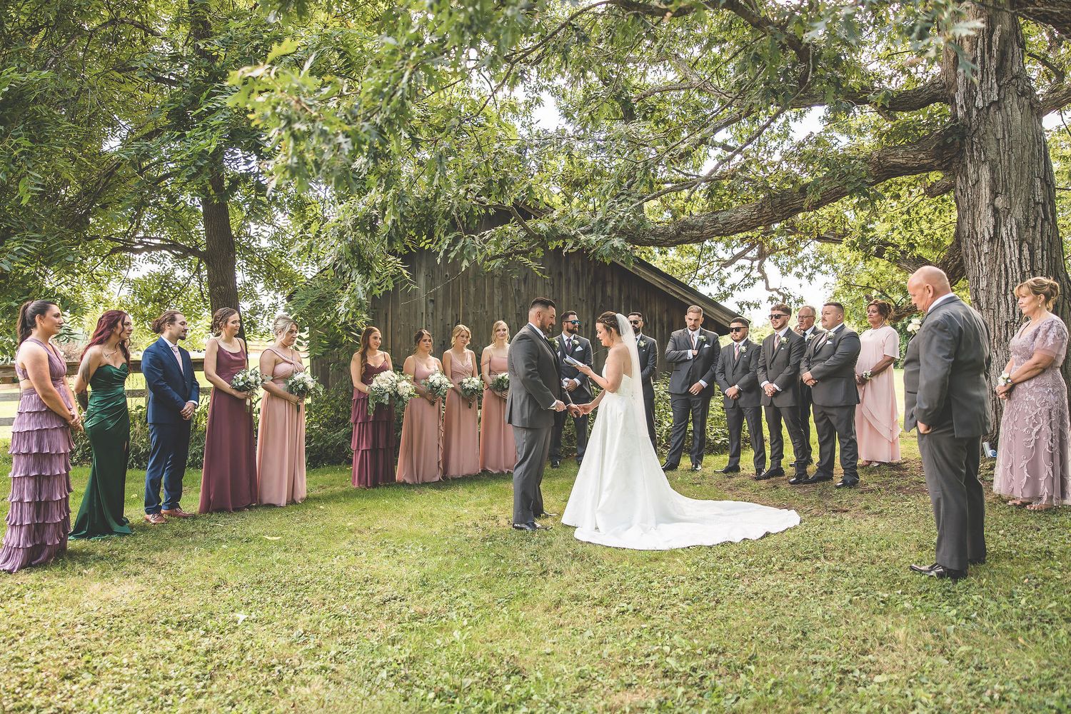 Wide shot of wedding guests lined up watching the outdoor ceremony near a rustic barn.
