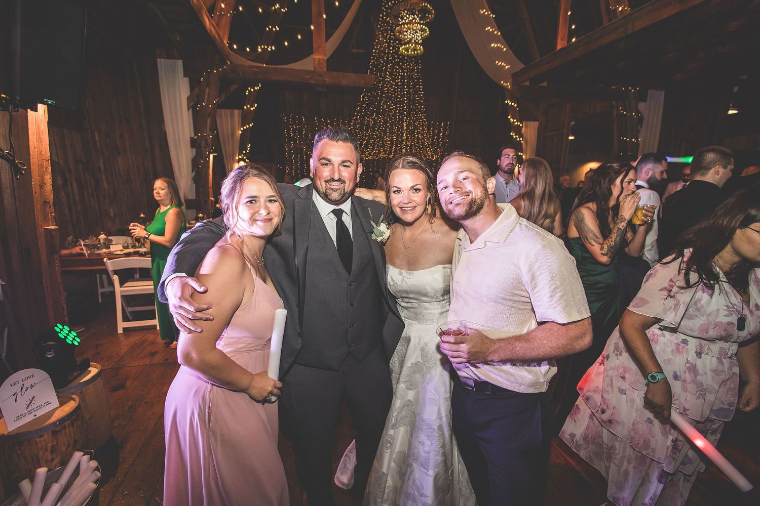 Wedding guests enjoying a lively dance party in a rustic barn venue with decorative lighting.