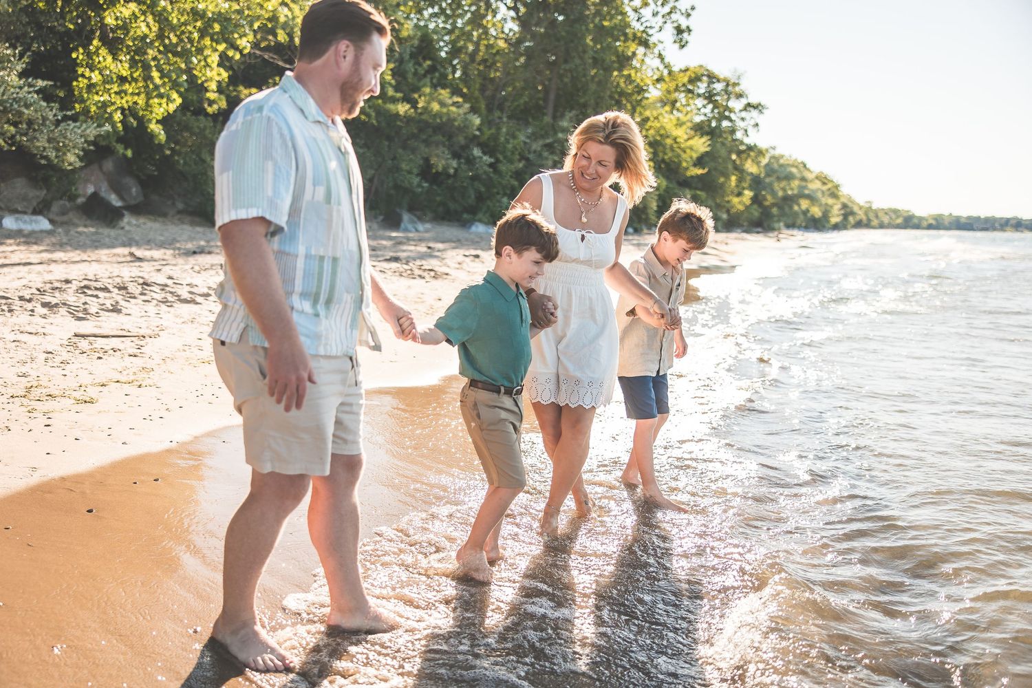 Family's feet splashing in shallow water at beach during golden hour.