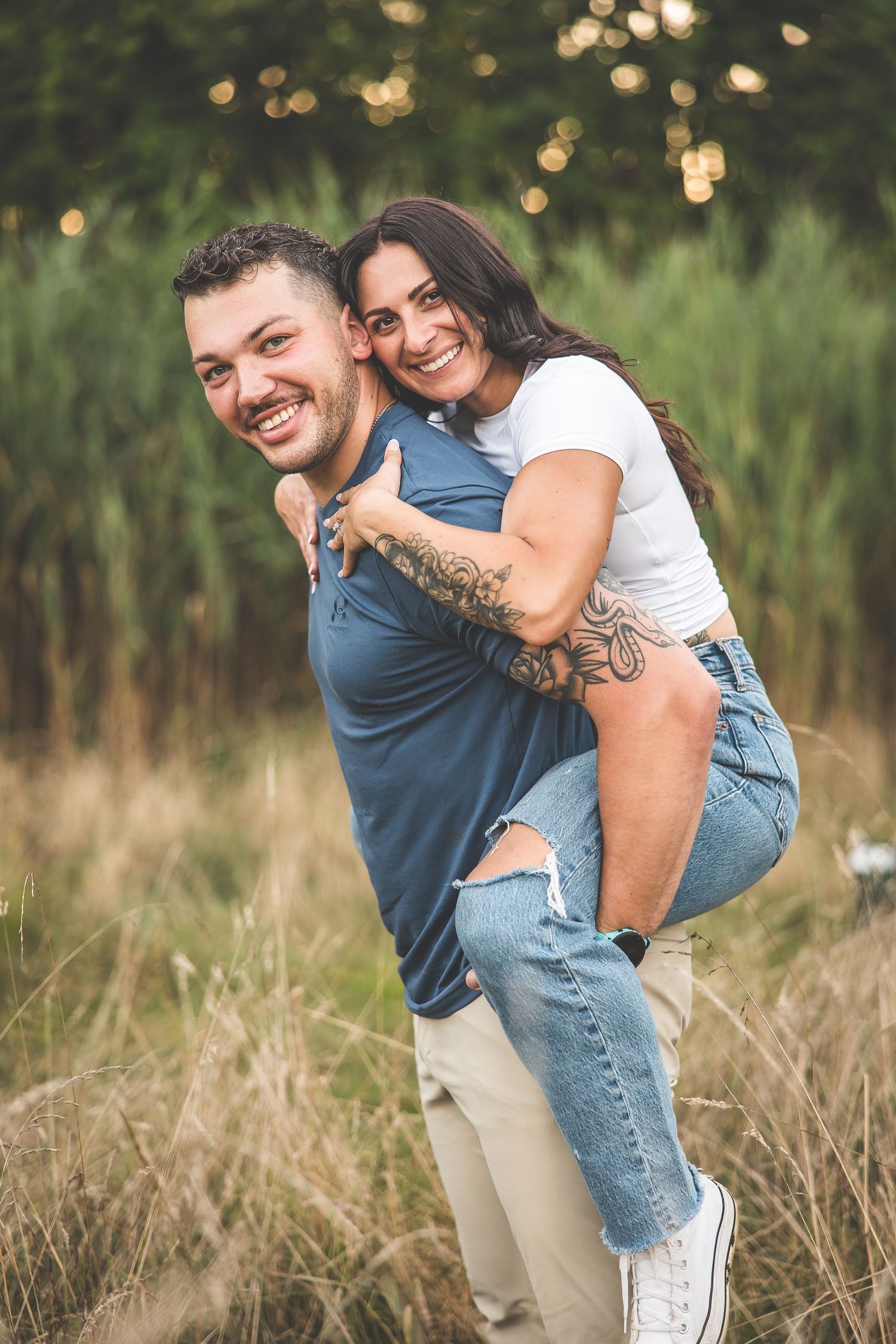 A couple playing and laughing together in a tall grass field during golden hour.