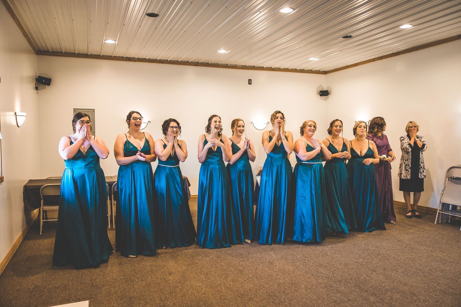 Bridesmaids in matching blue floor-length dresses stand in a line with hands clasped in excitement.