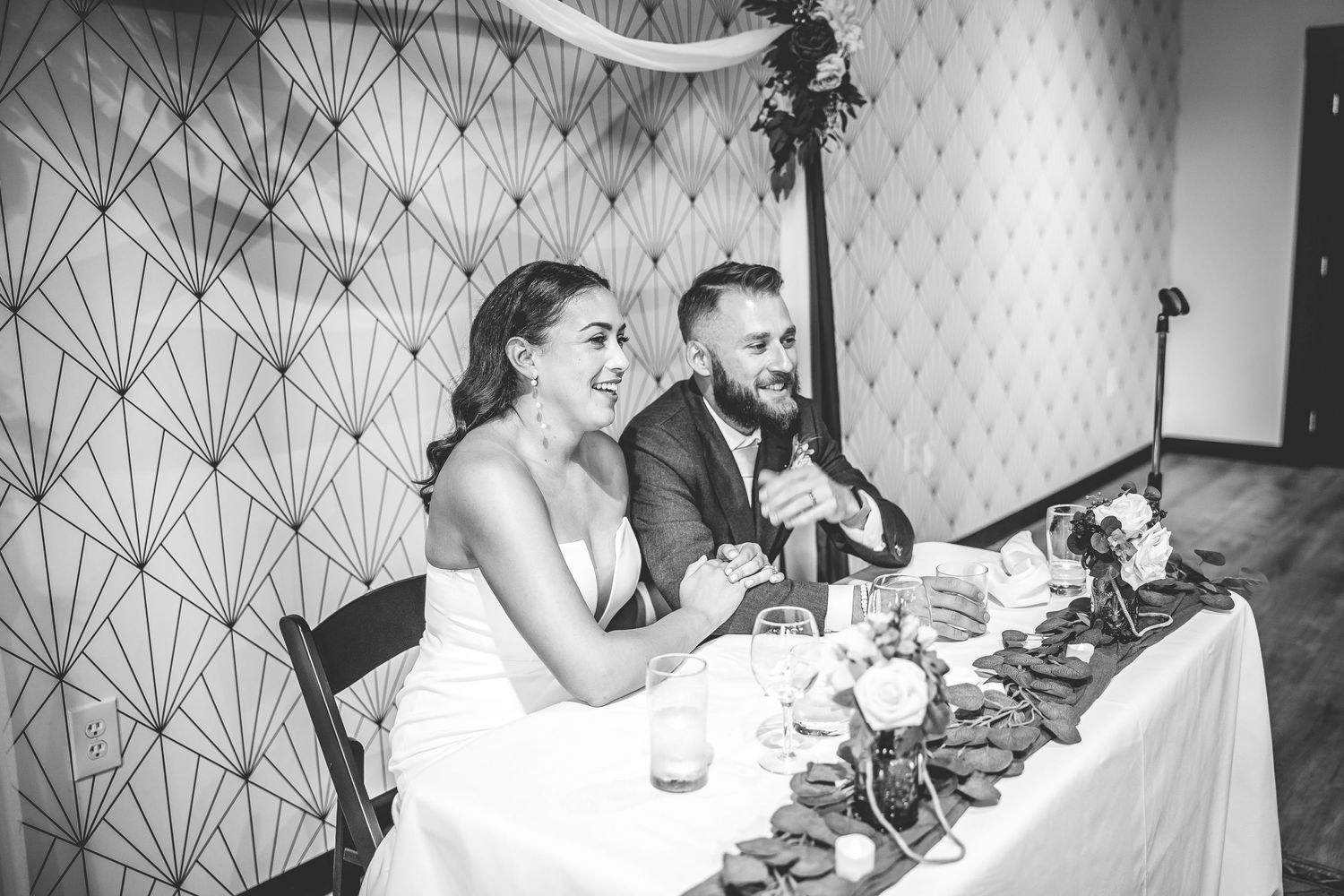 Black and white photo of couple enjoying speeches during wedding reception.
