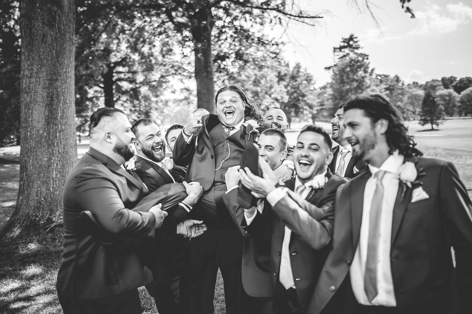 Groomsmen in navy suits laugh together during outdoor wedding photo session.