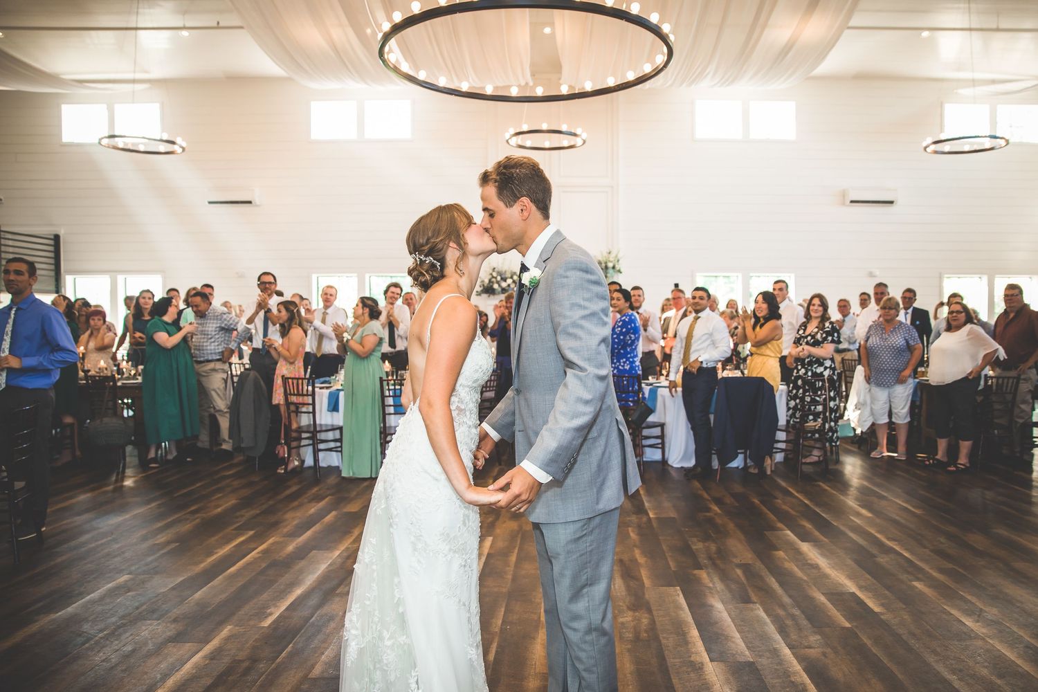 Wedding reception dance floor filled with guests celebrating under circular chandeliers.