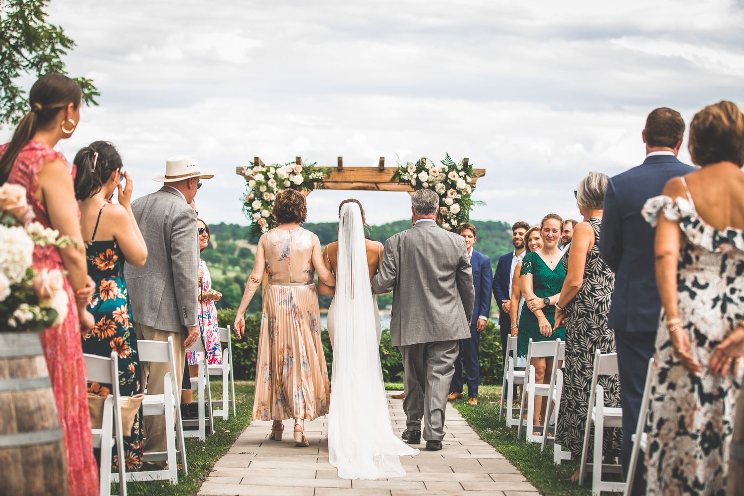 Wedding ceremony setup with white chairs and floral arch overlooking water.