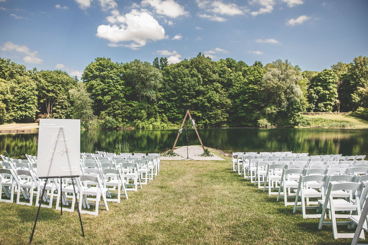 Outdoor wedding ceremony setup with white chairs on a grassy lawn overlooking a lake.
