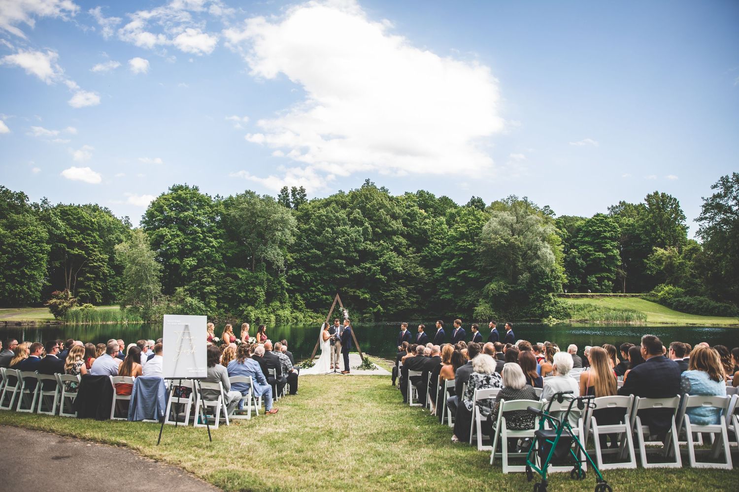 Panoramic view of wedding venue with white chairs set up under bright blue summer sky.