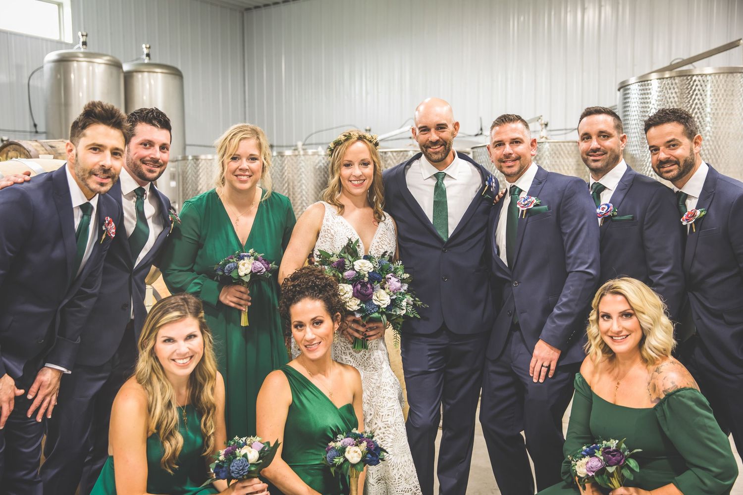 Wedding party poses together wearing navy suits and emerald green dresses.