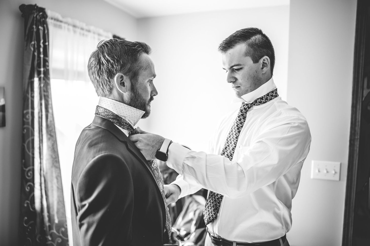 Two people in formal attire prepare for a wedding in a bright indoor setting.