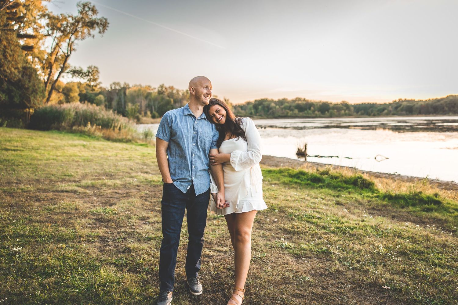 Romantic outdoor photoshoot in a grassy field near a serene lake during golden hour.