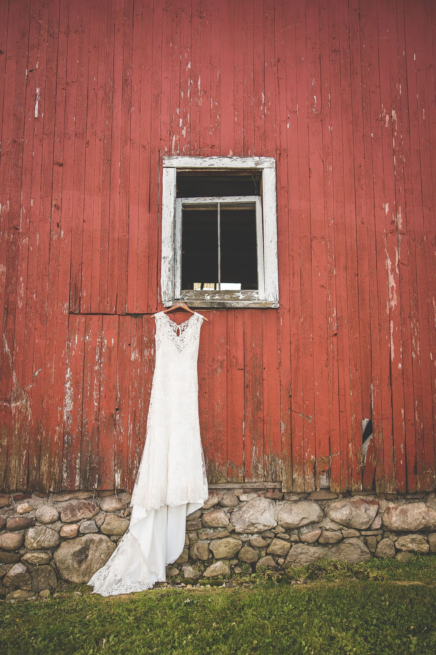 Weathered red barn exterior with stone foundation and white fabric decorations.