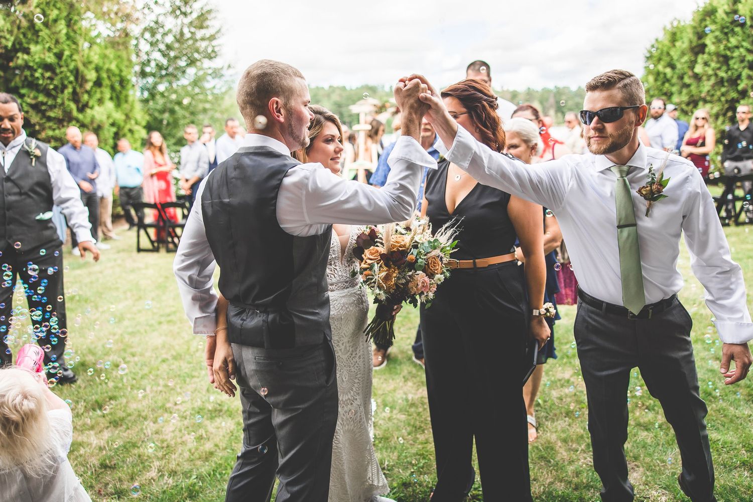 Celebratory moment with wedding party on sunny lakeside lawn.