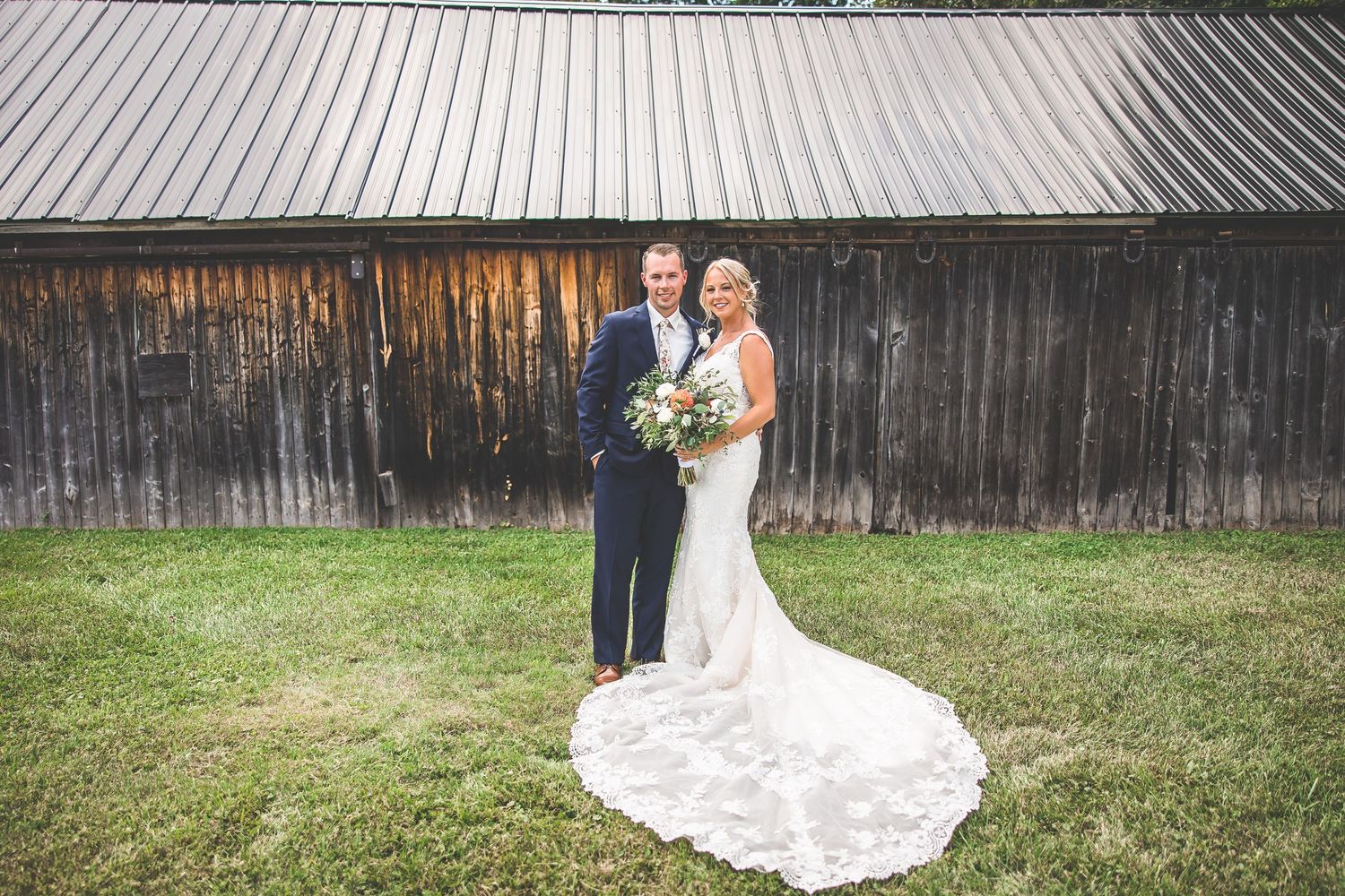 Wedding party poses for formal photos in front of a rustic wooden barn backdrop.