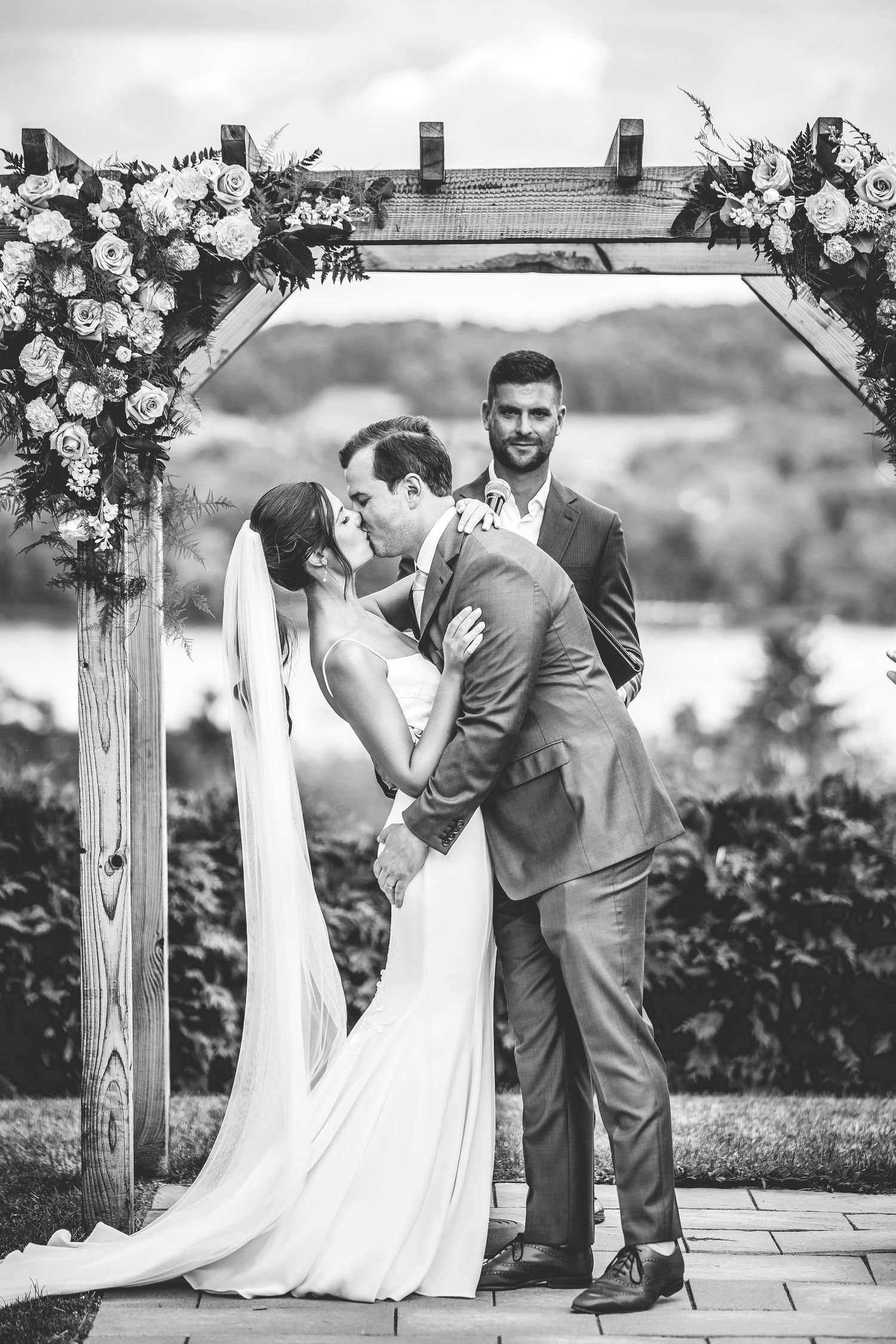 Black and white photo of intimate wedding ceremony moments under floral-decorated arch.