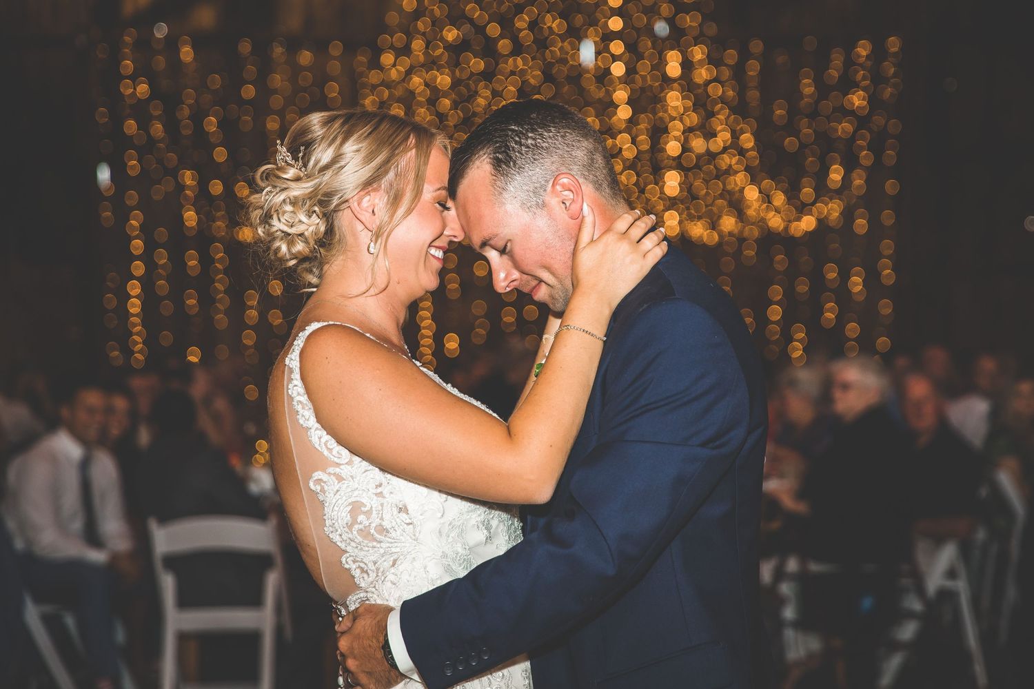Couple sharing an intimate dance moment under warm twinkle lights at their barn wedding reception.