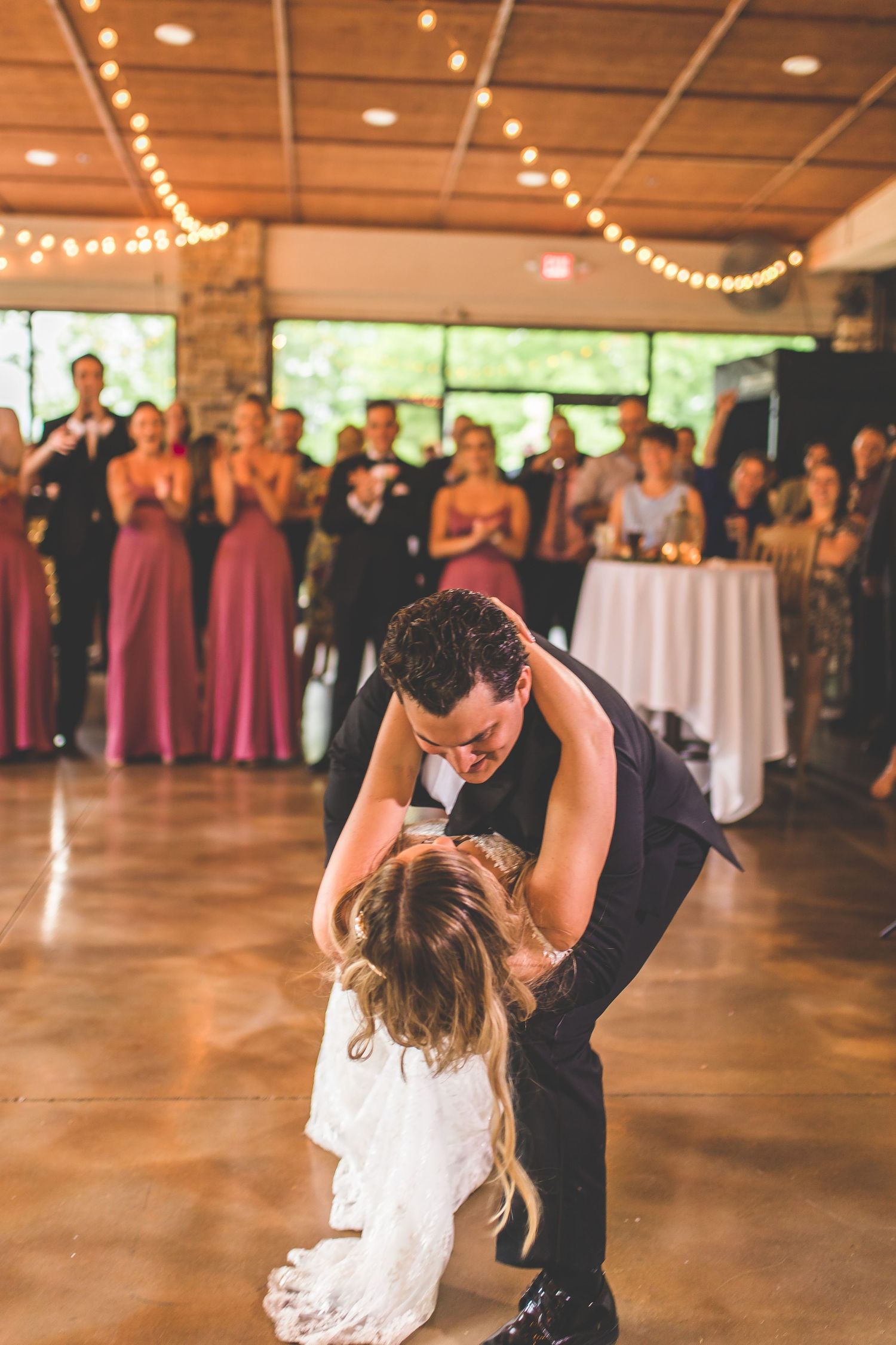 Wedding couple performs romantic dance in rustic reception venue with string lights.
