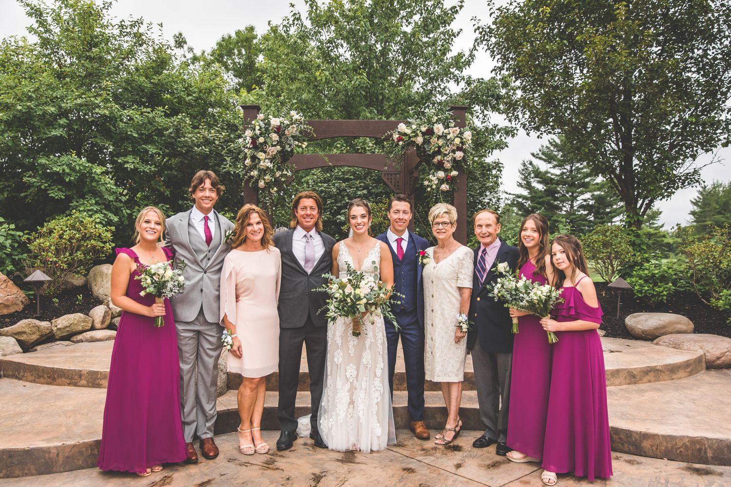 Extended family and wedding party group photo in outdoor garden setting.