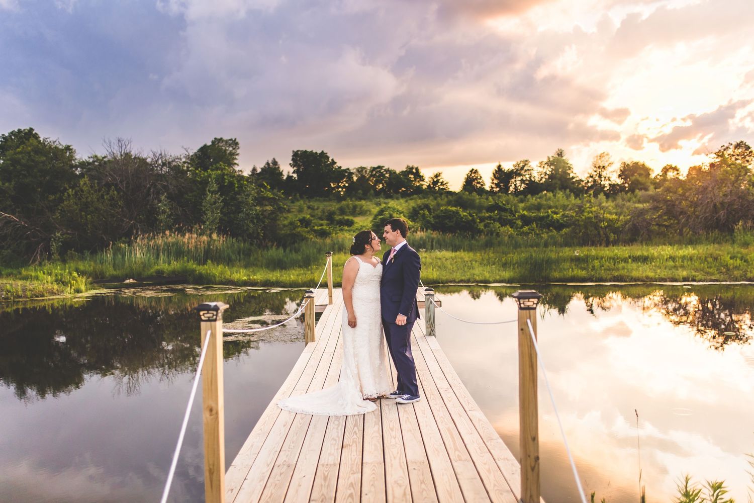 Couple poses on wooden dock during sunset by tranquil lake.