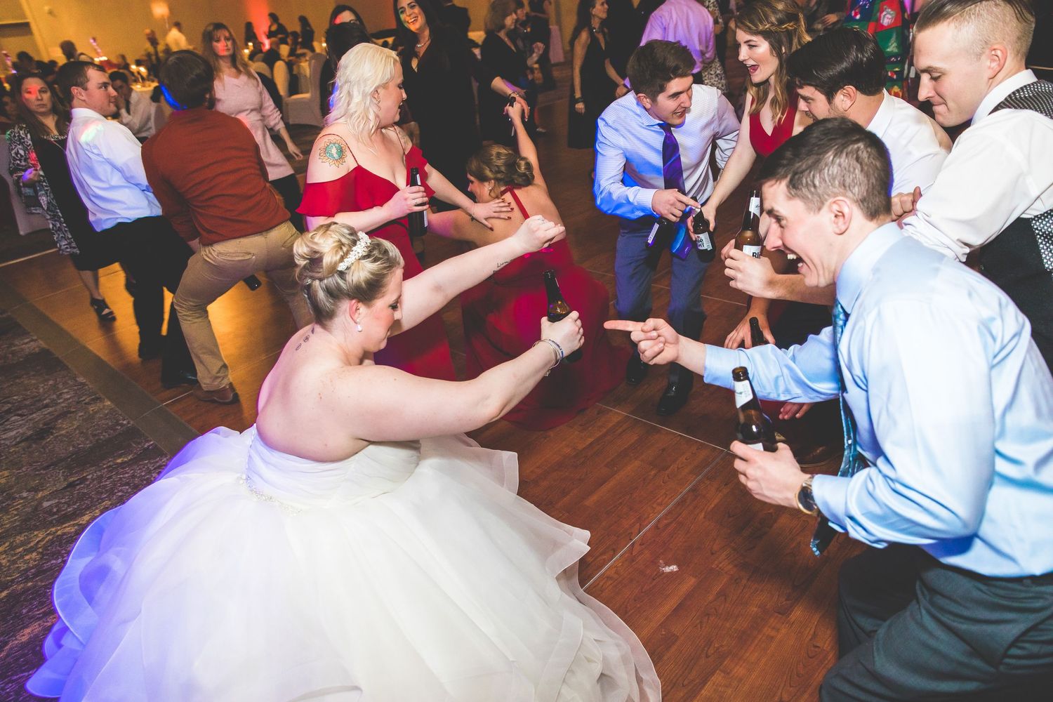 Wedding guests enjoying lively dancing and celebration on wooden dance floor at reception.