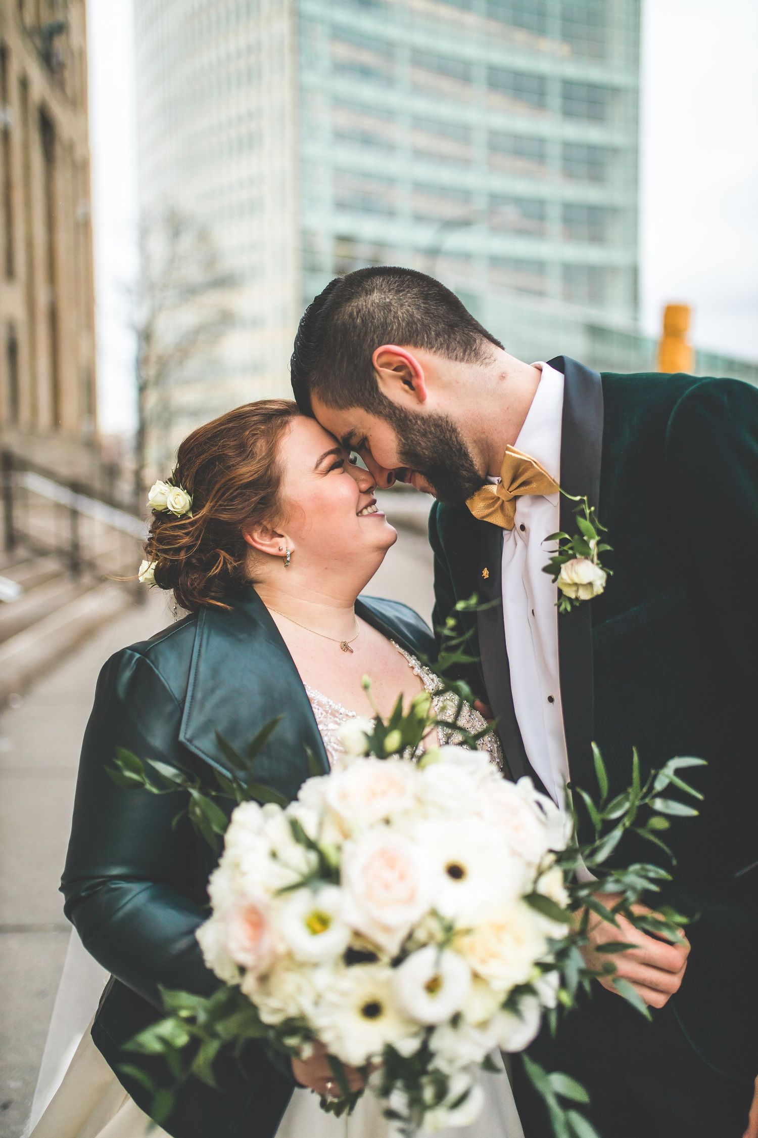 Wedding couple with white bouquet sharing romantic moments against urban backdrop.