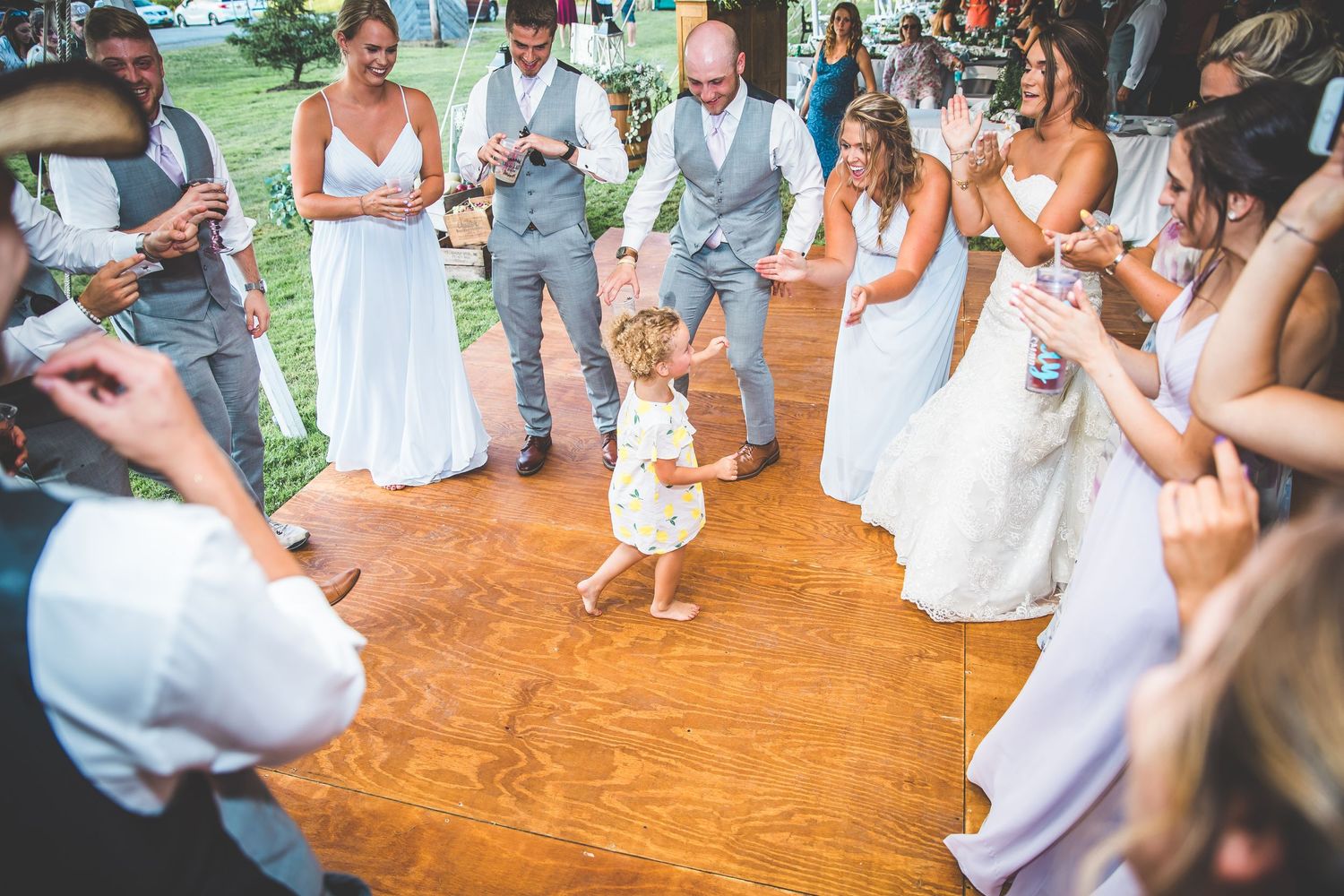 Wedding guests dancing and celebrating on a wooden dance floor at a reception.