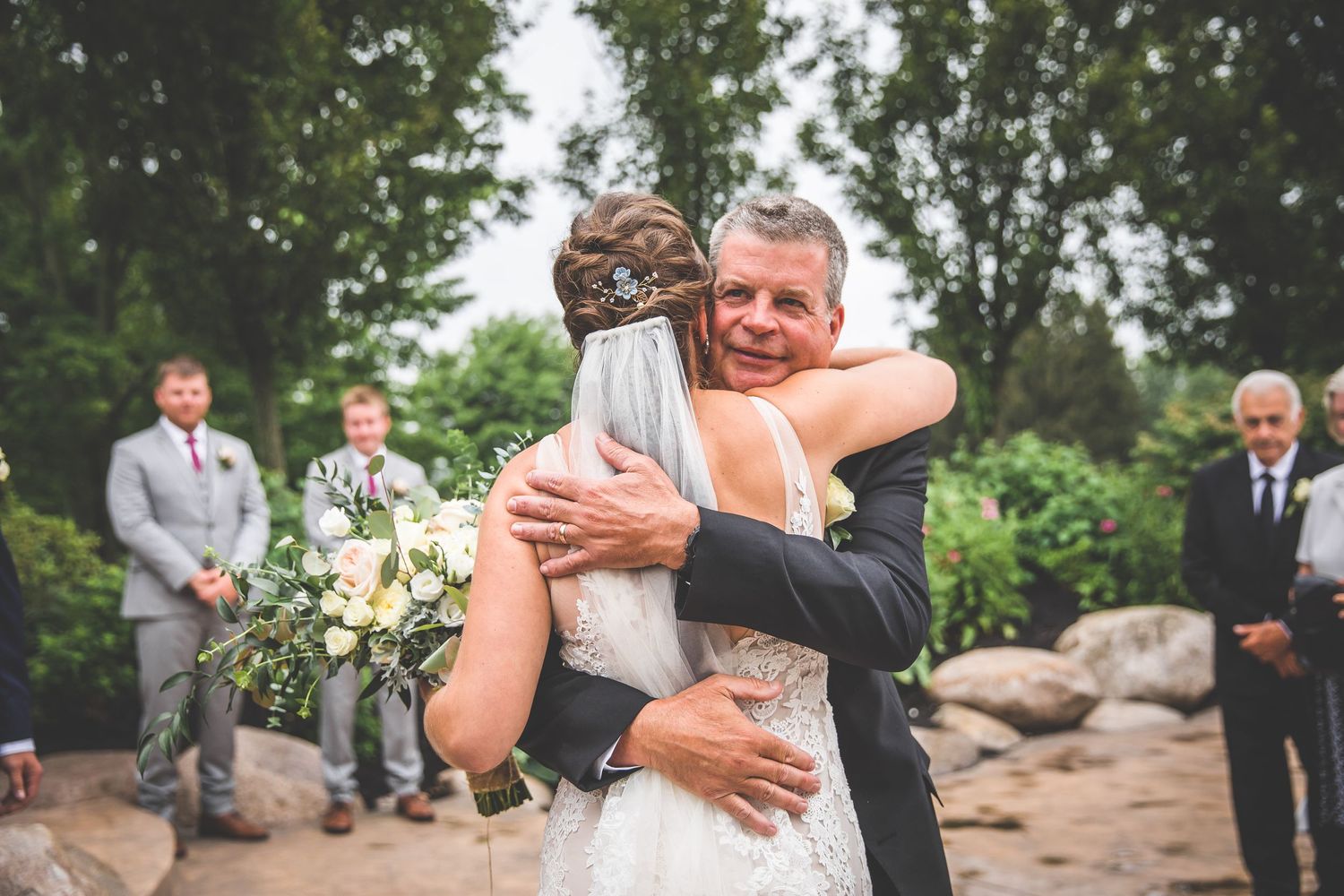 Emotional moment during outdoor wedding ceremony with natural greenery backdrop.