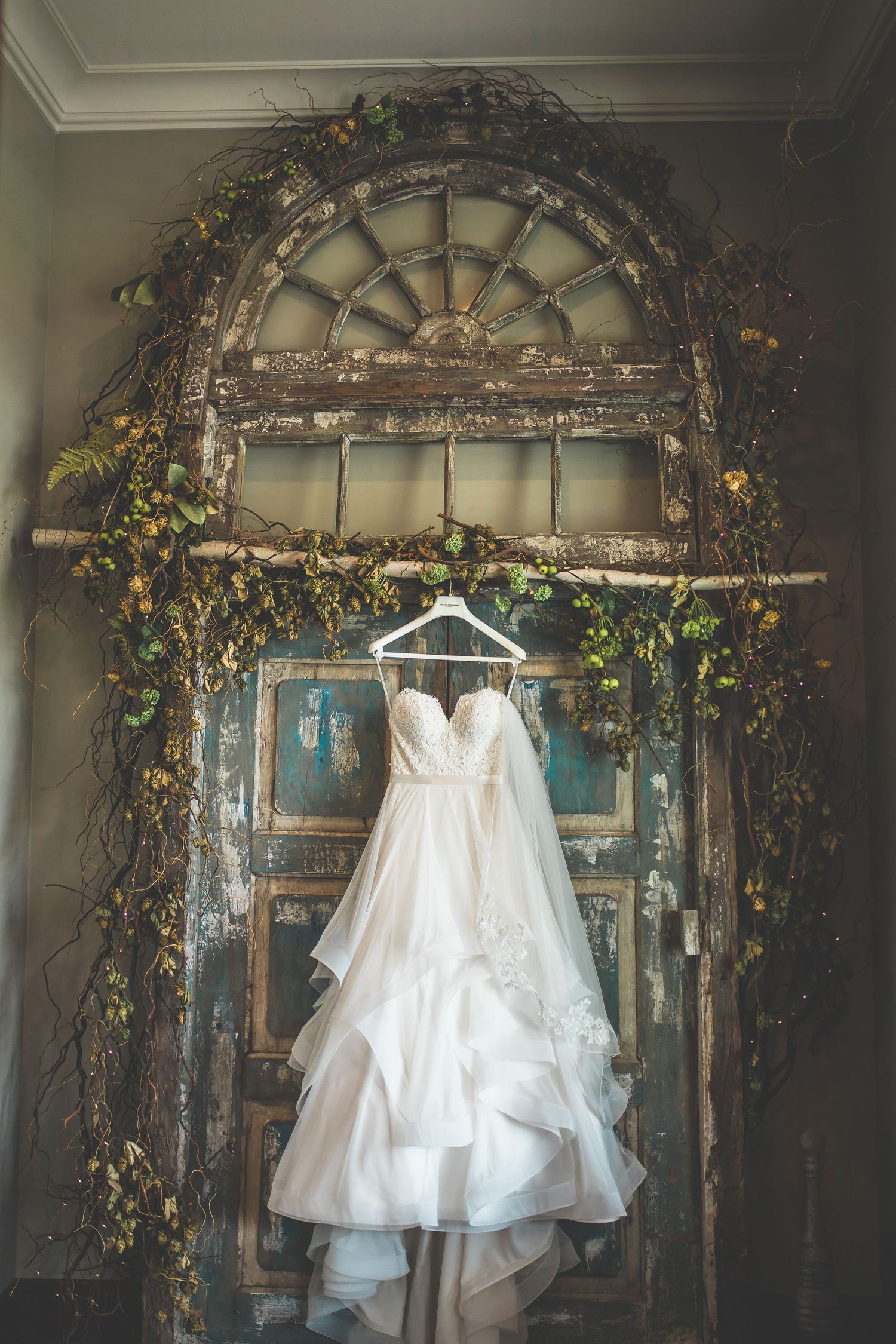 A white wedding gown hangs beneath an ornate archway decorated with vintage-inspired floral arrangements.
