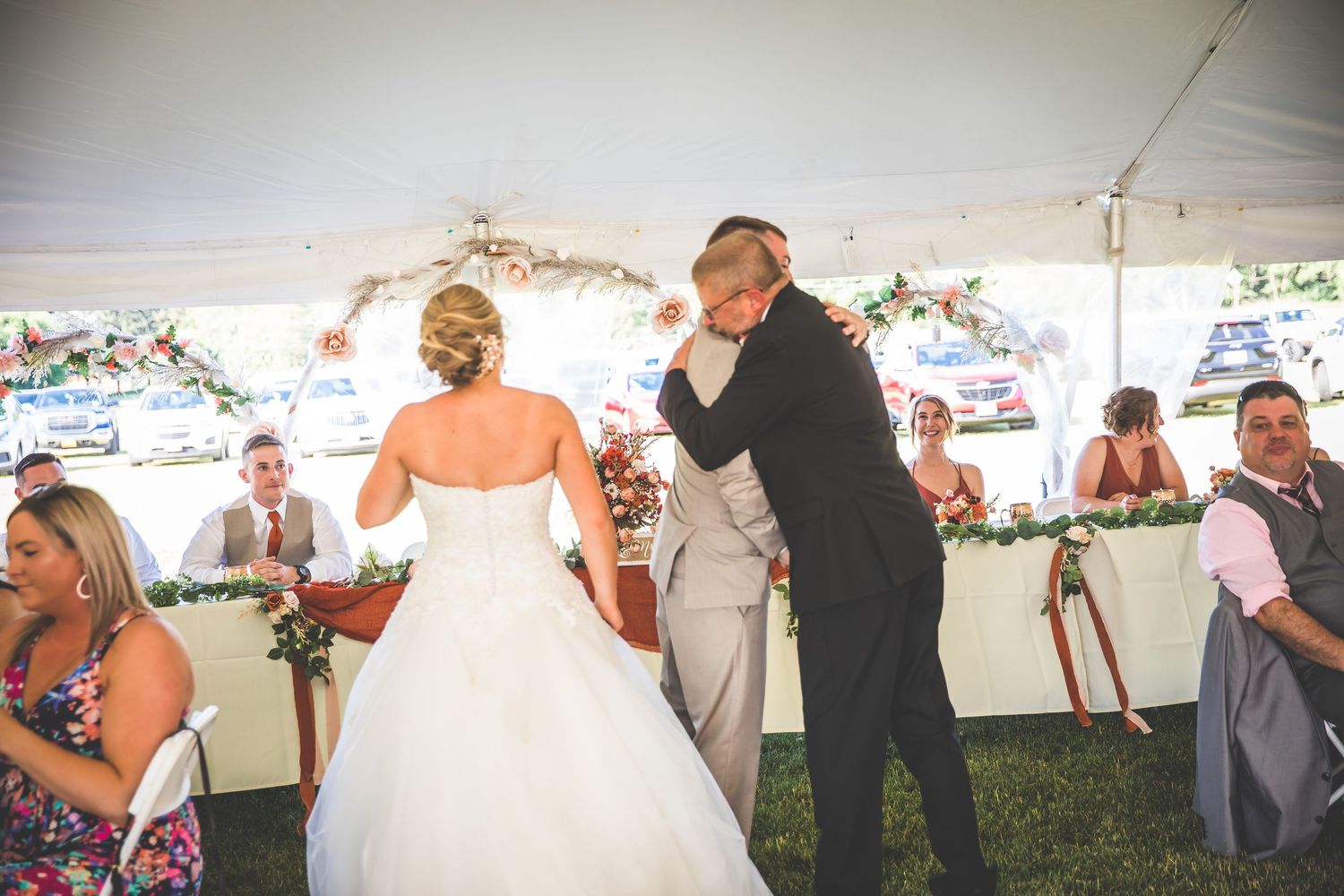 Wedding reception dance party in full swing under decorated outdoor tent with guests looking on.
