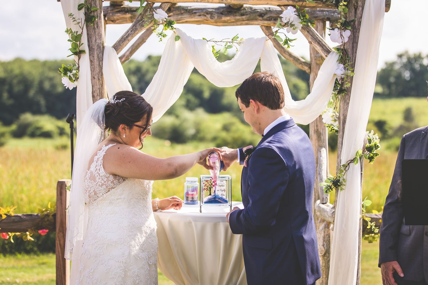 Wedding ceremony taking place under a rustic wooden arch decorated with white fabric.