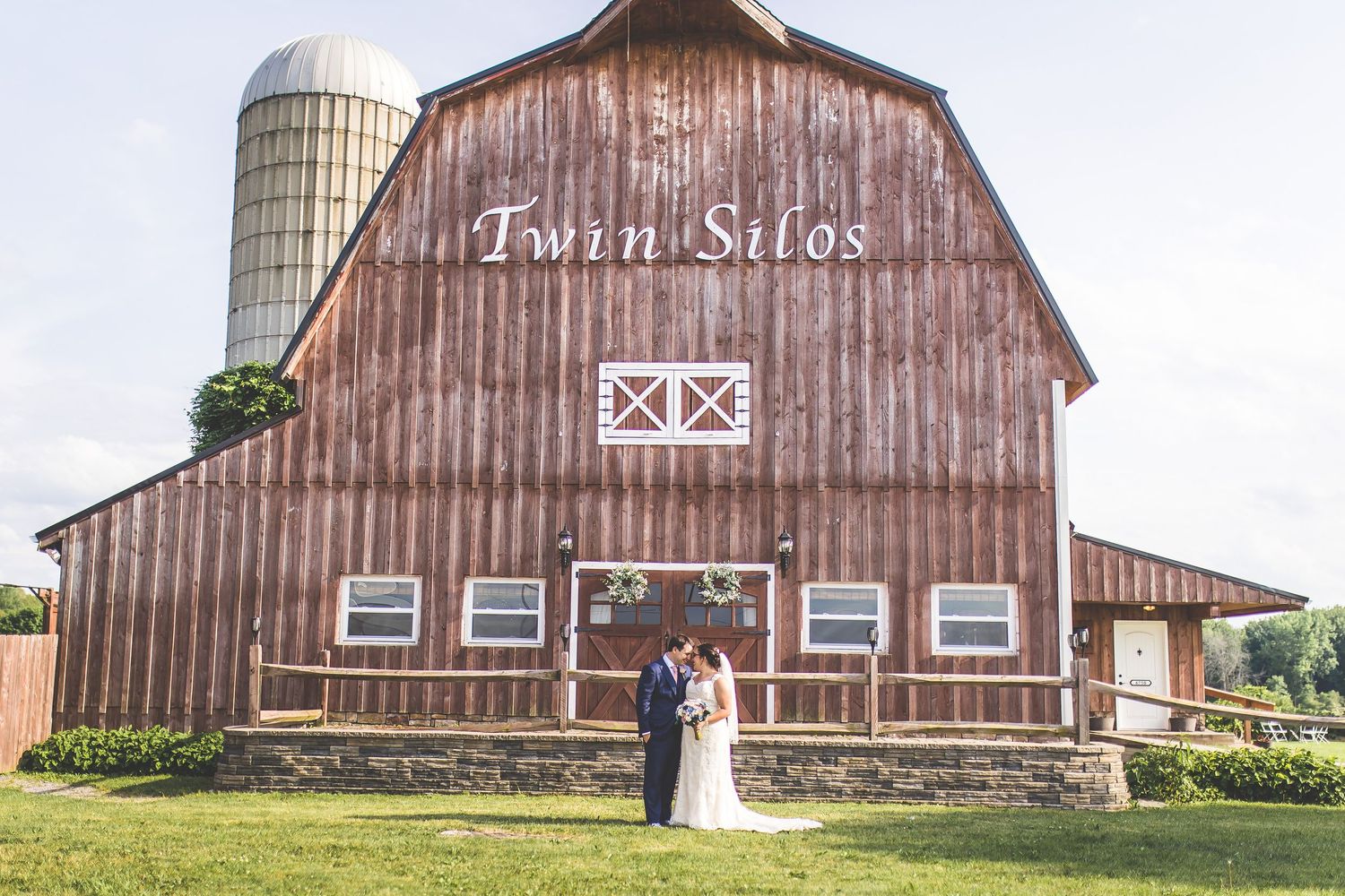 Rustic brown barn exterior with white trim and silos photographed in a panoramic style.