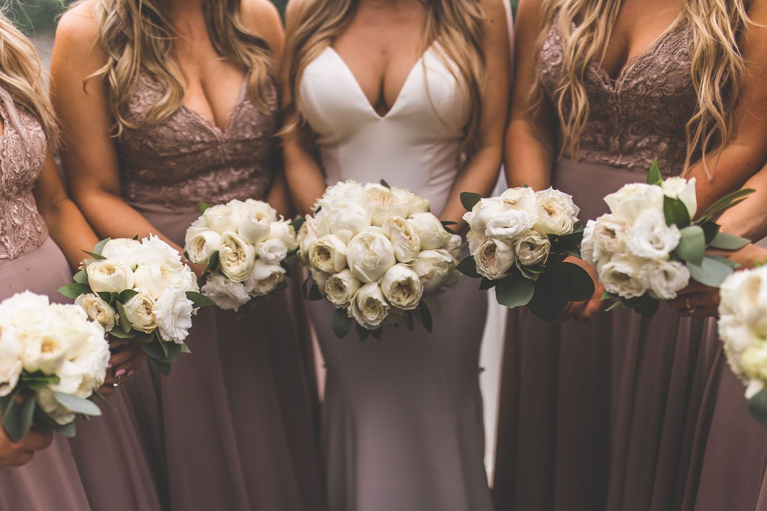 Close-up of wedding party holding white rose bouquets against mauve bridesmaid dresses.