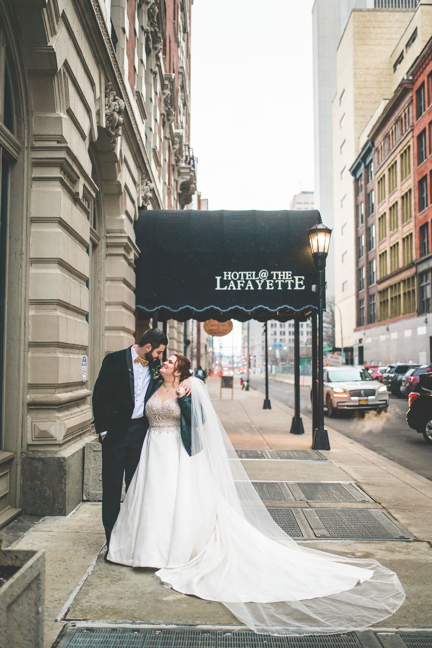 Elegant wedding photo under the Hotel Lafayette entrance canopy with flowing white dress train.