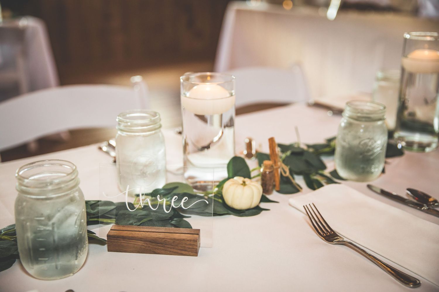 Wedding reception table settings with mason jars and eucalyptus garland decor.