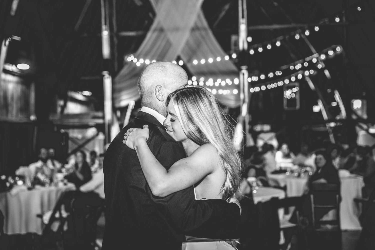 Wedding reception dance floor with string lights hanging overhead in a rustic barn venue.