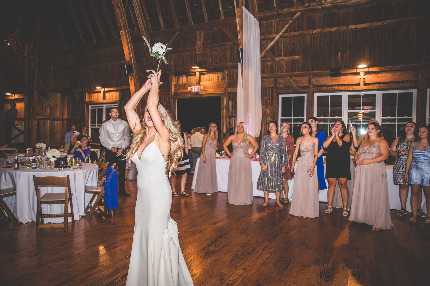 A bride tosses her bouquet to waiting guests at a rustic barn wedding reception.