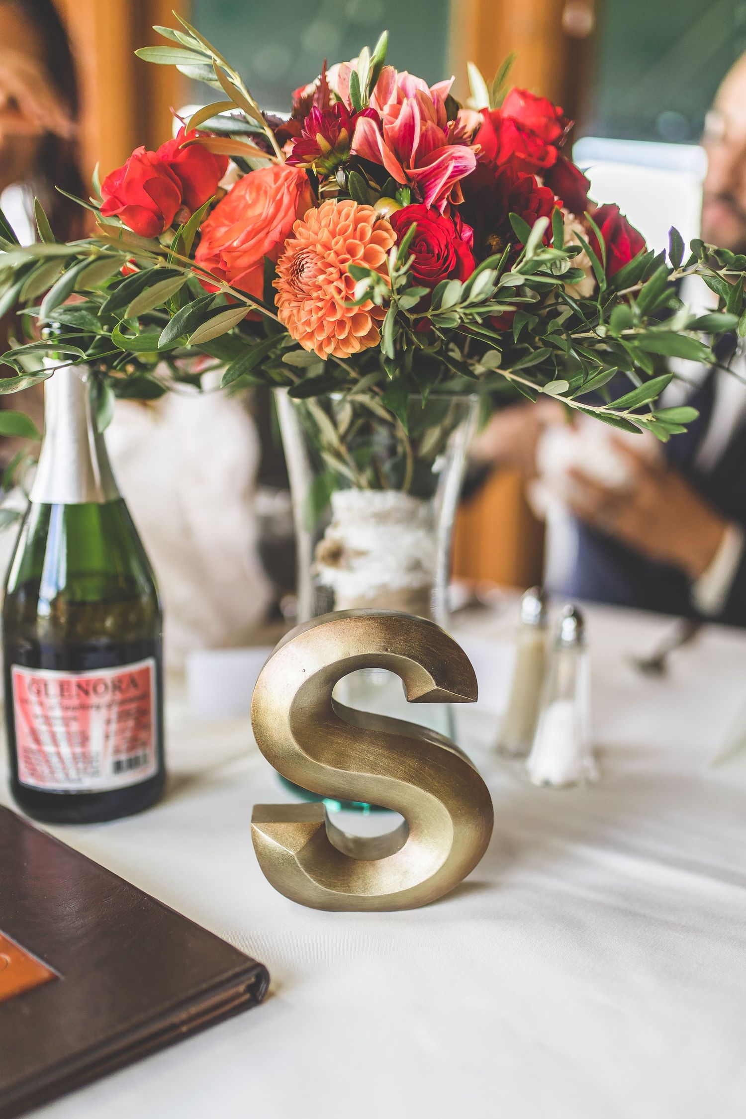Wedding table decor featuring red and orange flower arrangements with gold letter accents.