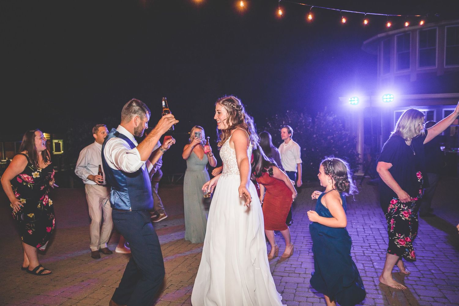 Guests dance under purple and blue lighting at a nighttime wedding reception.