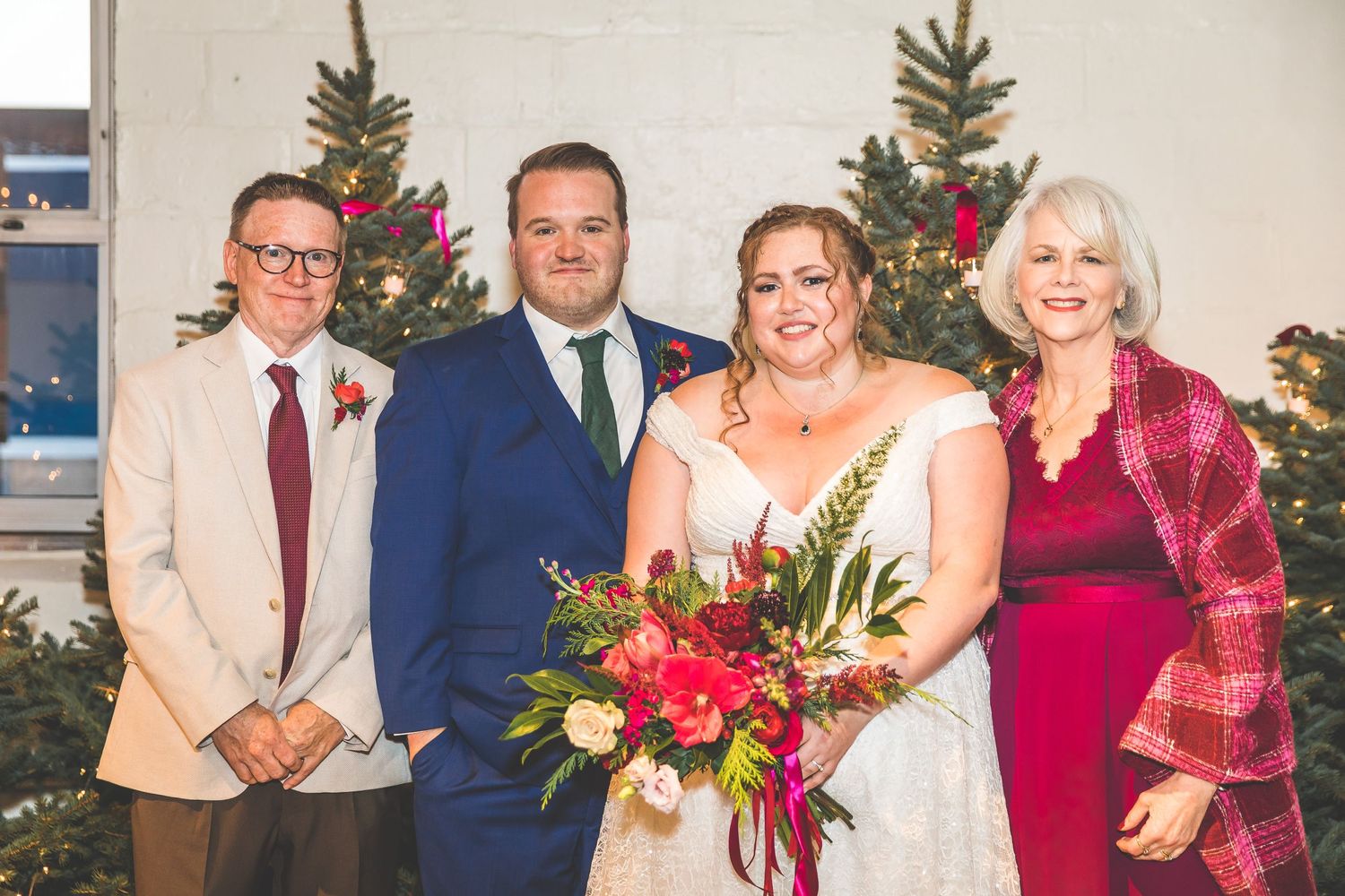 Wedding party members pose in formal attire with festive holiday decorations and Christmas trees in the background.