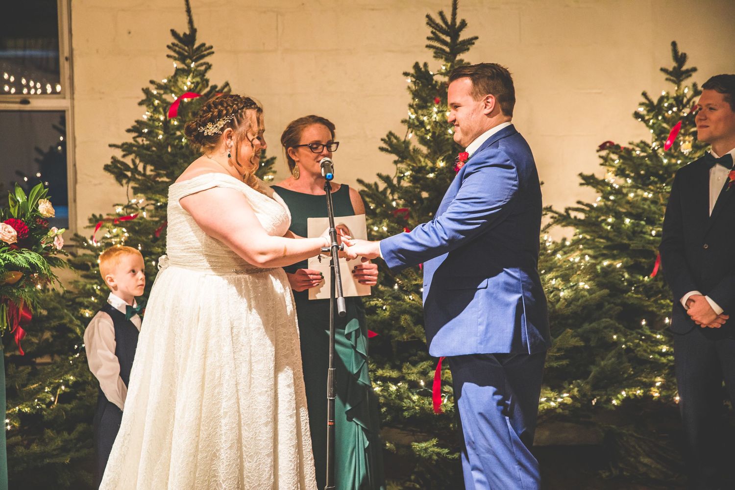 A couple exchanges vows during their winter wedding ceremony with Christmas trees in the background.