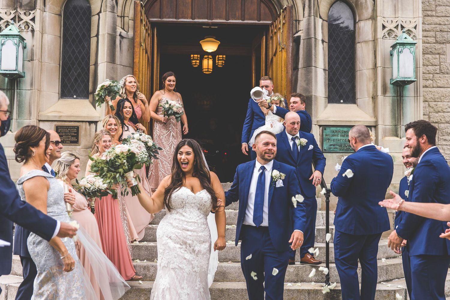 Joyful wedding celebration on church steps with guests in blue and pink attire.