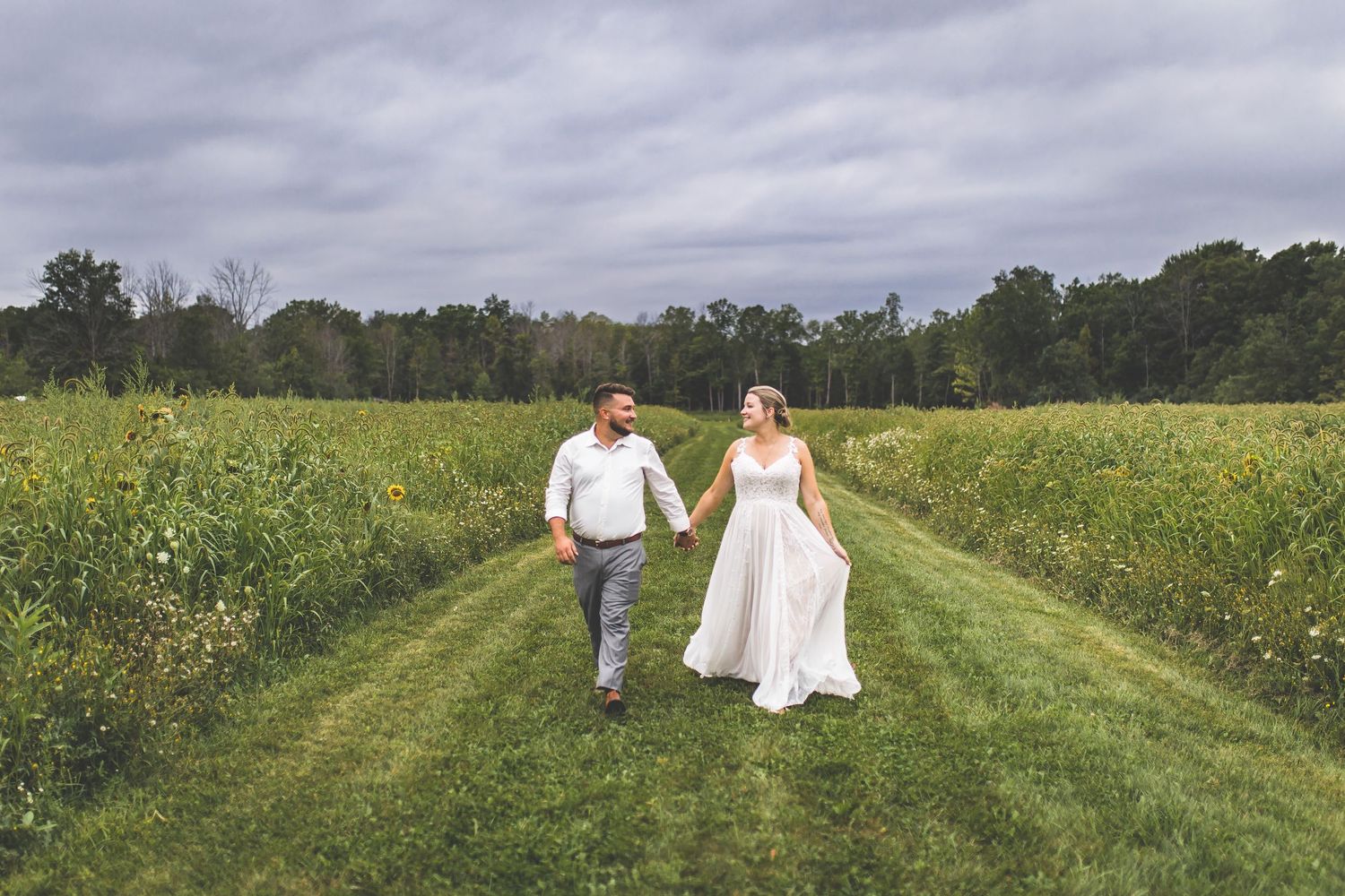 A couple walking hand in hand down a grassy path between wildflower fields.