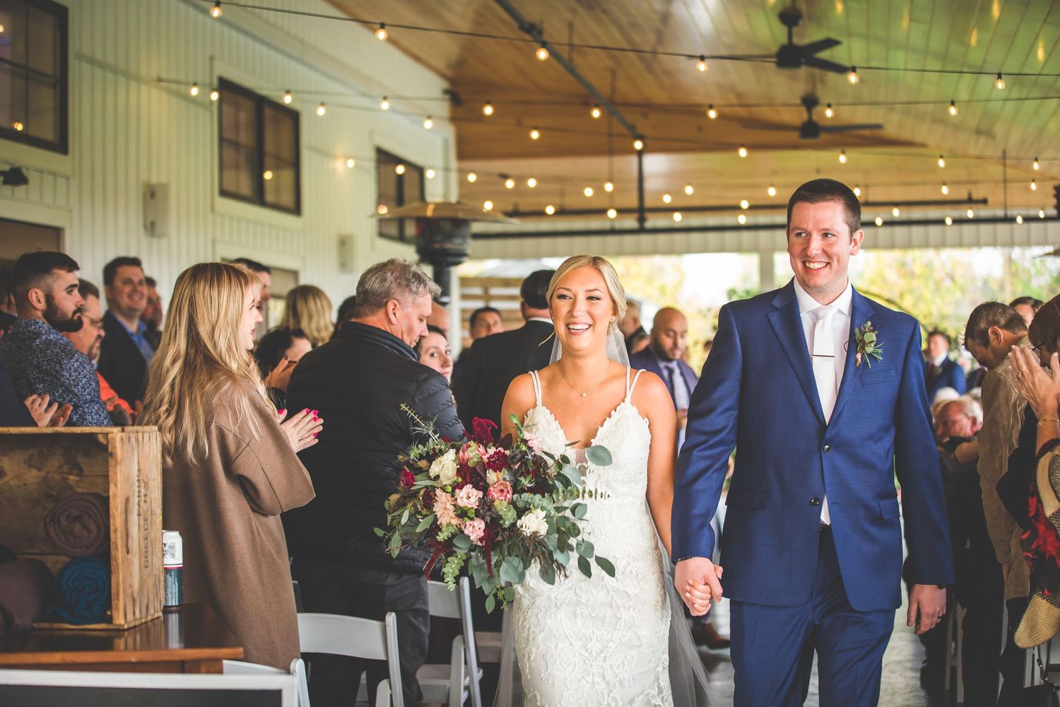 Wedding recessional in modern venue with guests applauding as couple walks down aisle.