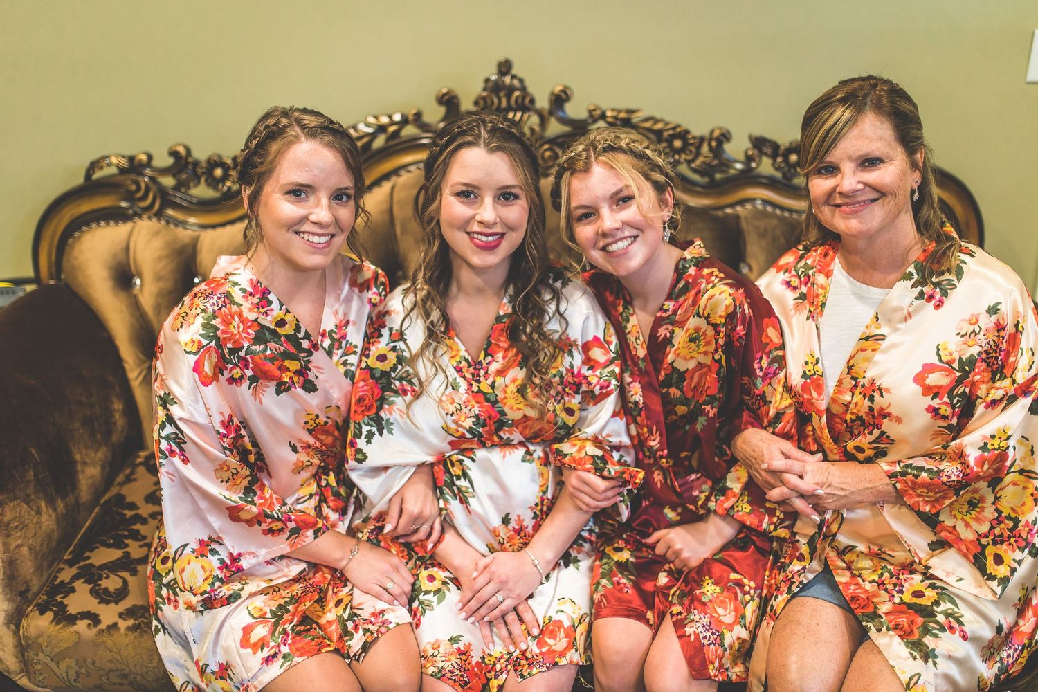 Wedding party in matching floral robes posing on vintage sofa during pre-ceremony preparations.