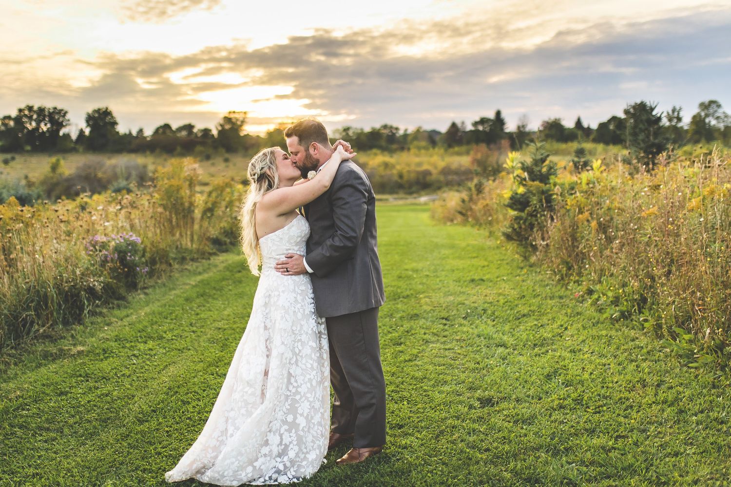 Romantic sunset portraits on grassy path with dramatic sky backdrop.