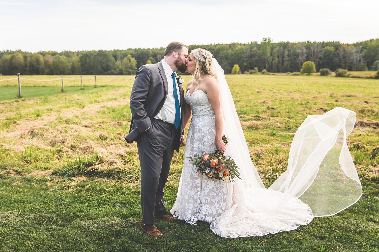 Wedding photography session in rustic field with dramatic veil movement.