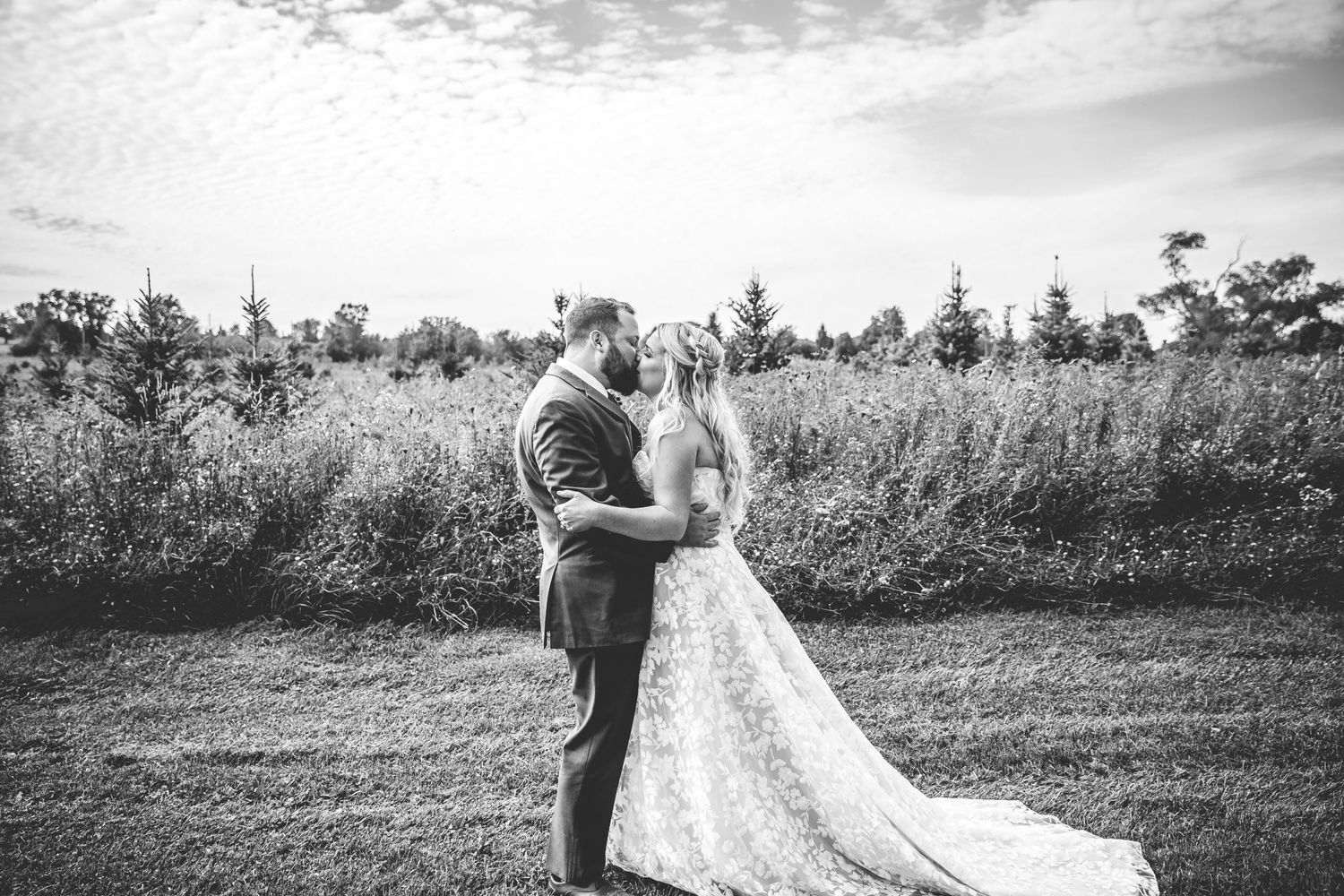 Black and white wedding portrait captured in a rustic outdoor setting with natural lighting.