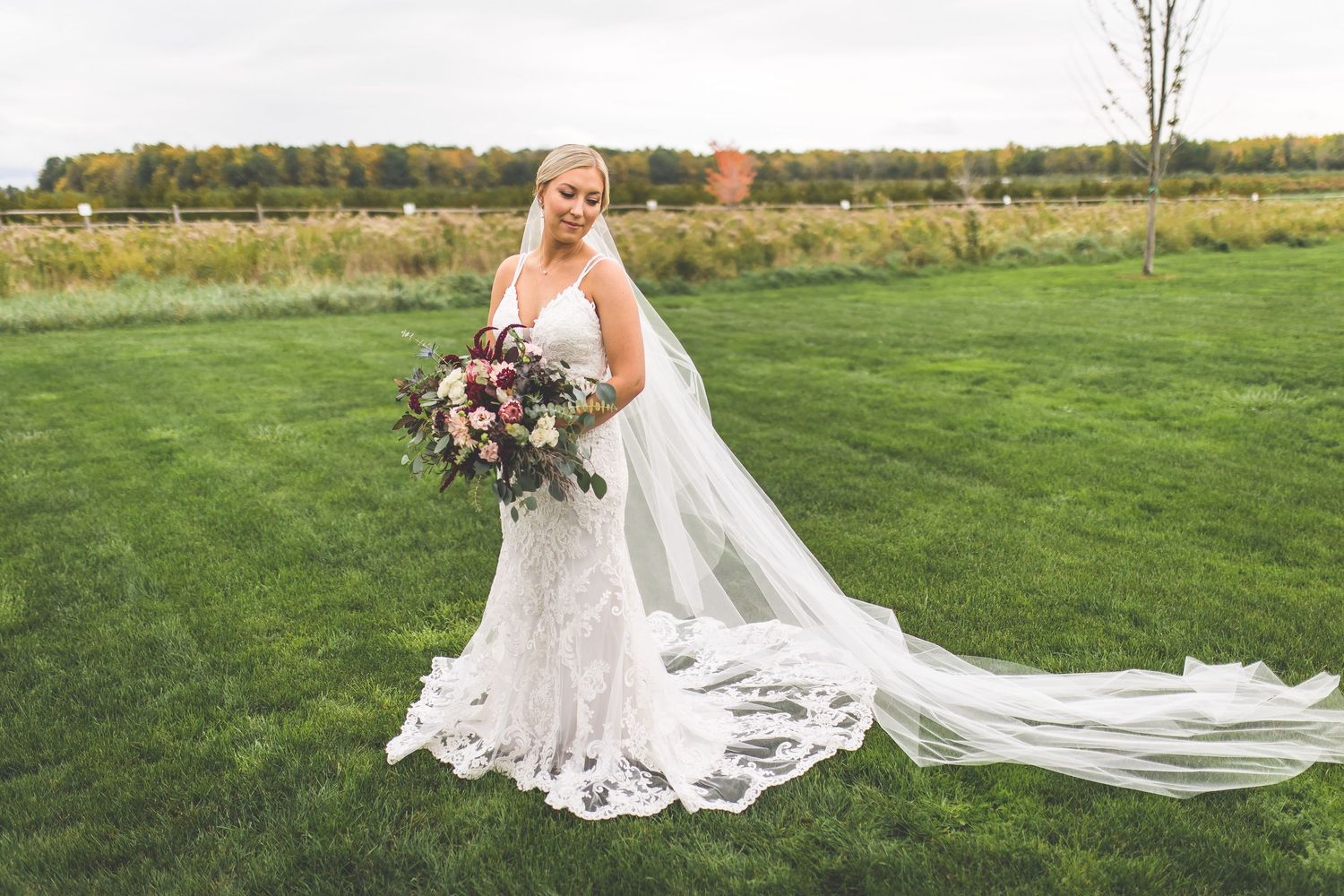 A bride in a flowing lace dress poses in a scenic autumn field.