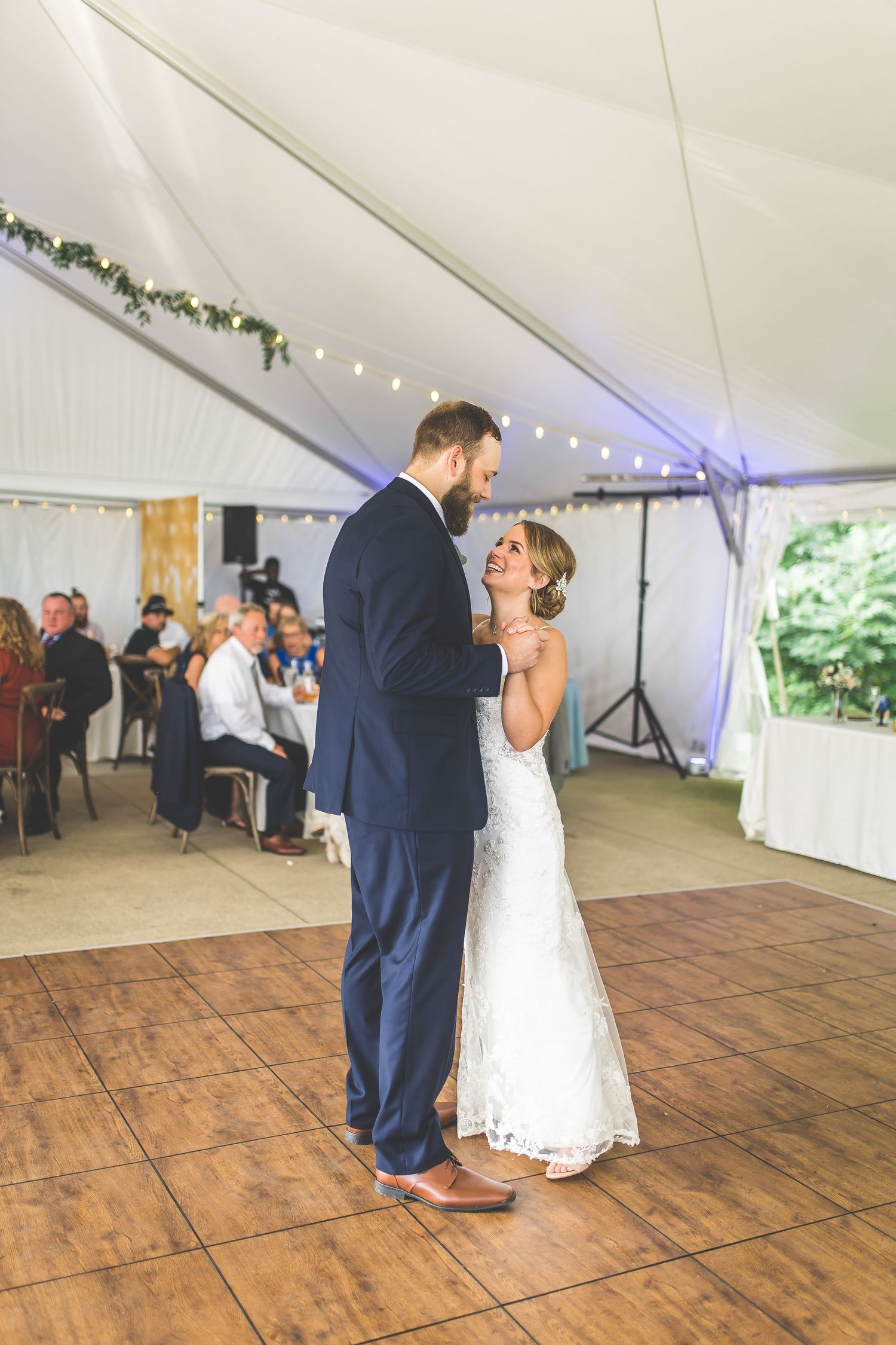 Newlyweds share an intimate dance moment on a wooden dance floor under a decorated tent.
